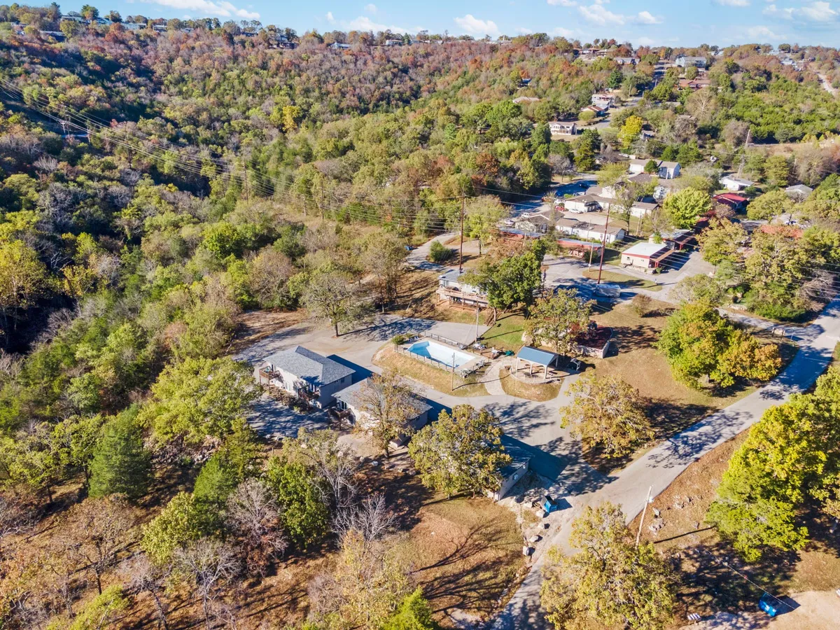 This exterior shot highlights the resort-style community grounds, featuring wooden structures, a swimming pool, shaded walkways, and mature trees. The scene is lively yet peaceful, ideal for activities like walking or playing with a dog.