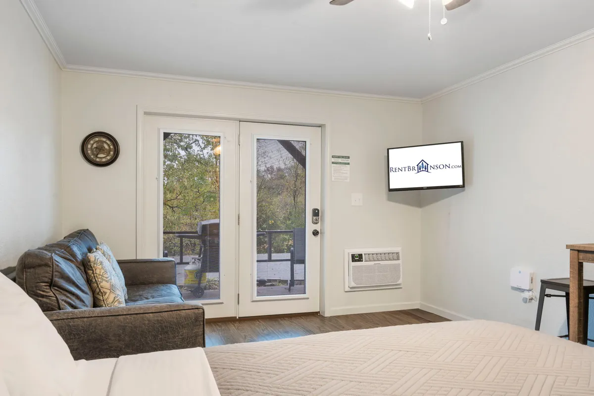 This interior image features a comfortable living space with a sofa, bed, TV, and doors leading to a balcony. The setup feels relaxed and serene, and the direct access to the outdoor balcony hints at easy indoor-outdoor living, important for pet owners.