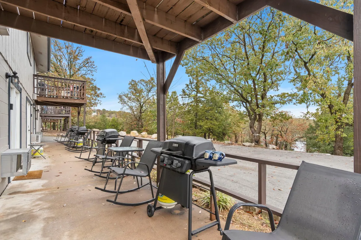 The image features an inviting outdoor area with grills, rocking chairs, and a scenic view of nature. The seating area faces out toward open green space, suggesting relaxation and casual gatherings in a pet-welcoming environment.
