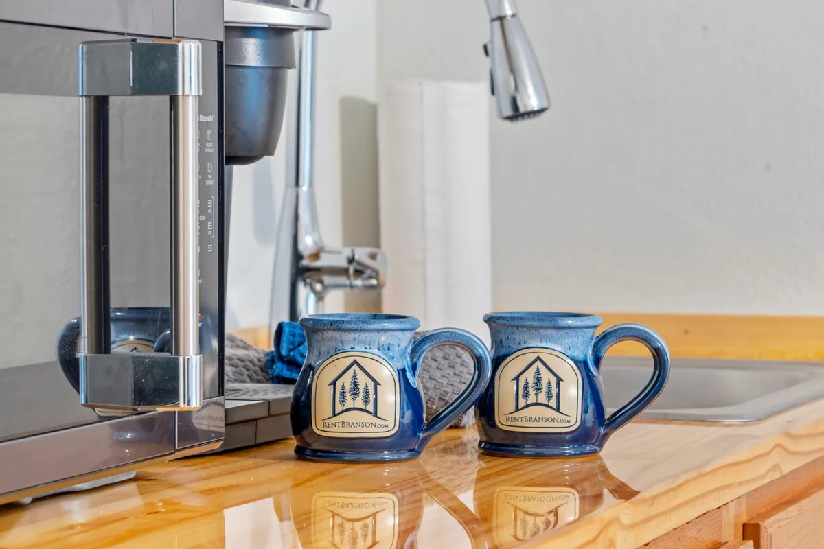 The image showcases a cozy kitchenette area featuring blue ceramic mugs beside a coffee maker on the counter, complemented by a stainless steel sink. The setup invites guests to imagine starting their mornings with a fresh brew, setting a welcoming and homey tone for their stay.