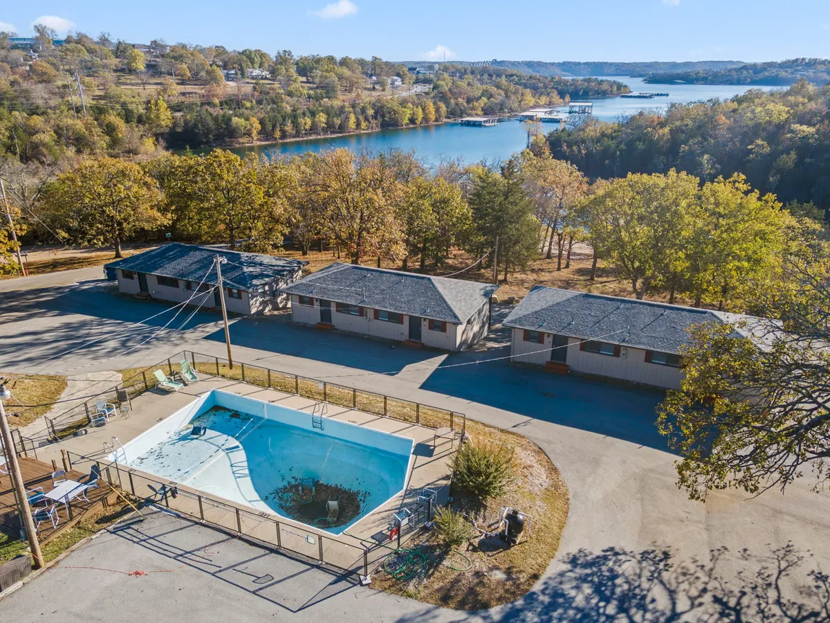 This image presents a serene exterior view of a swimming pool adjacent to a lake, with lush trees and motel units in the background. The setting exudes tranquility and offers ample green space for walks and outdoor relaxation.