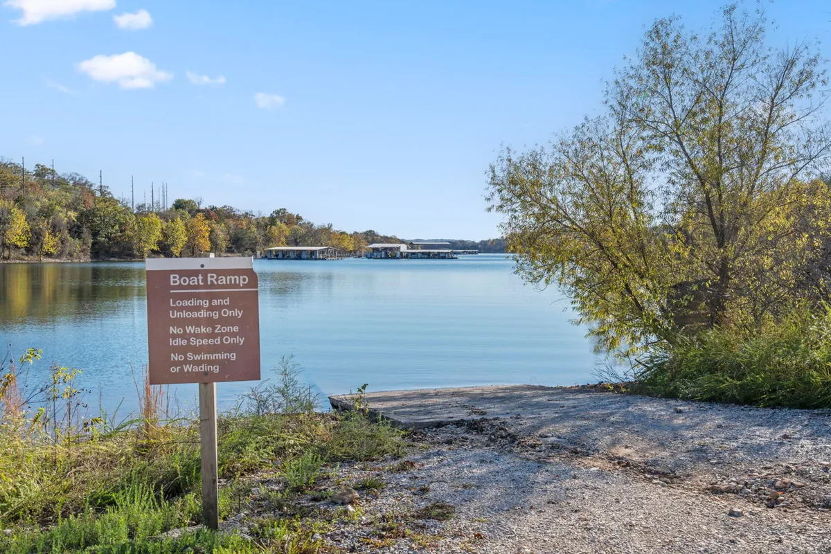 A panoramic view of a boat ramp leading into tranquil lake waters, bordered by trees. Subtle signage and natural surroundings suggest easy access to boating, fishing, or simply watching the sunset together.